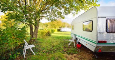 Caravan trailer on a green lawn under the trees, on a sunny Autumn day. France