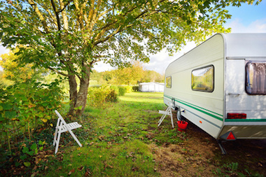 Caravan trailer on a green lawn under the trees, on a sunny Autumn day. France